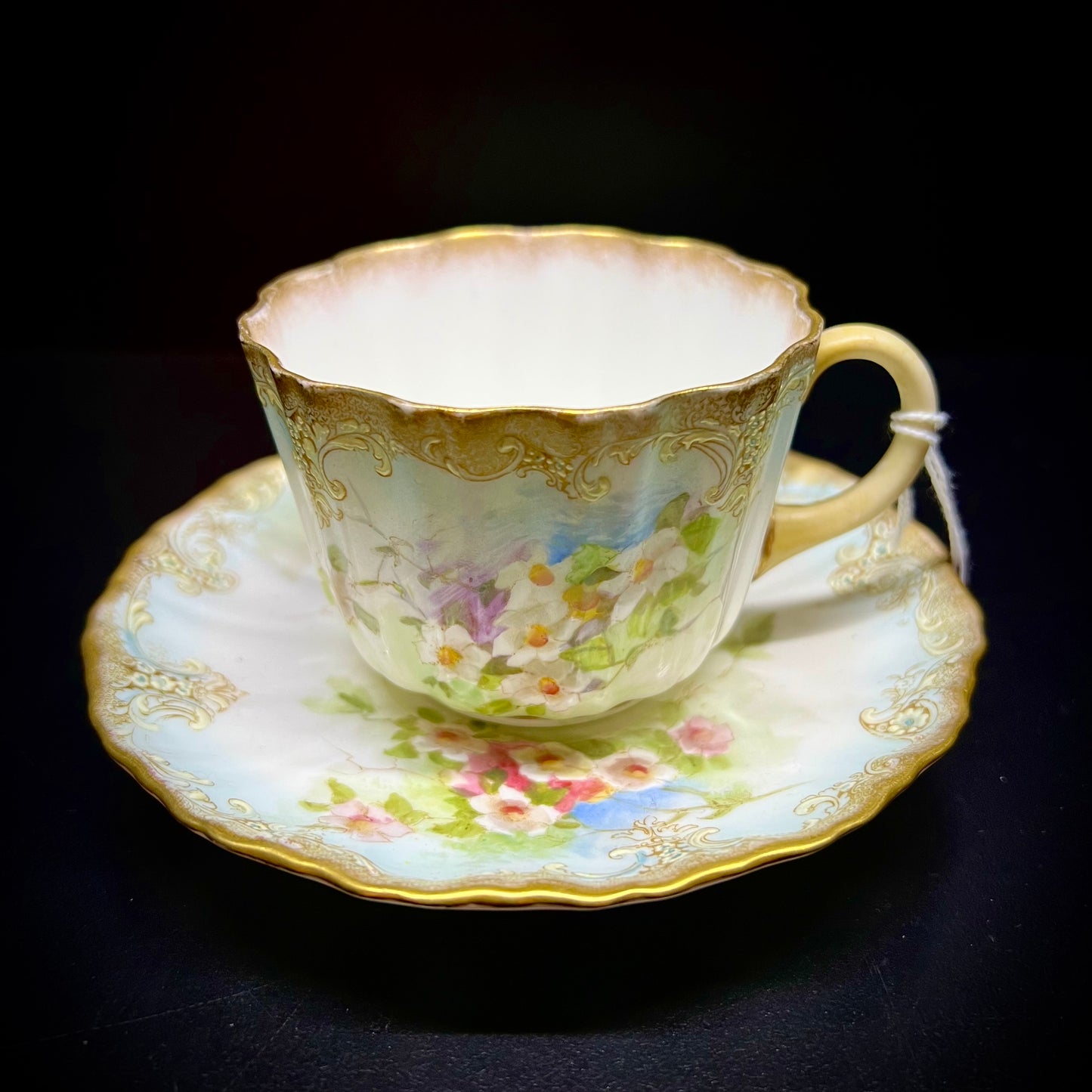 Victorian teacup and saucer decorated with rich bouquets of white flowers and raised enamel