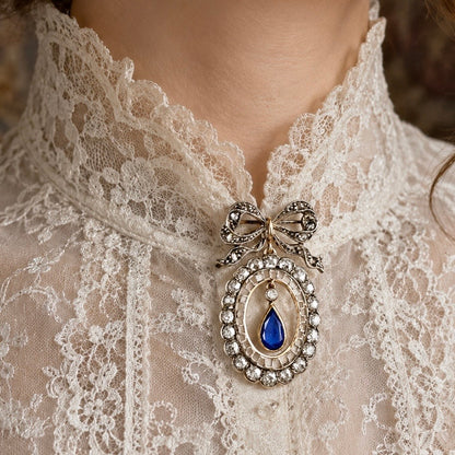 Deliziosa spilla Belle Époque in oro con fiocco, diamanti old mine e zaffiro pendente